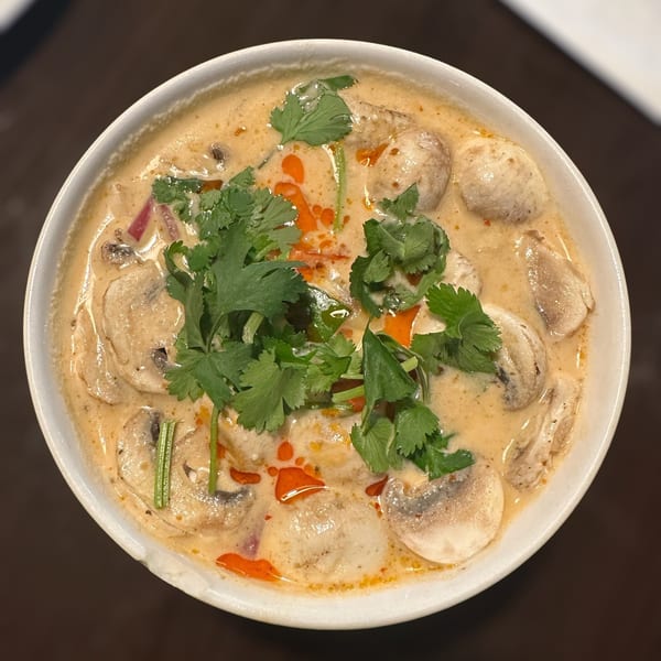 Bowl of creamy Thai soup with mushrooms, sliced vegetables, chili oil, and fresh cilantro garnish.